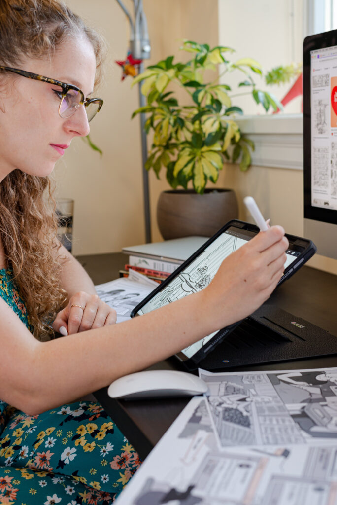 Image of Jen Backman, illustrator from Inky Thinking sitting at desk with stylus in right hand, working on digital illustration.